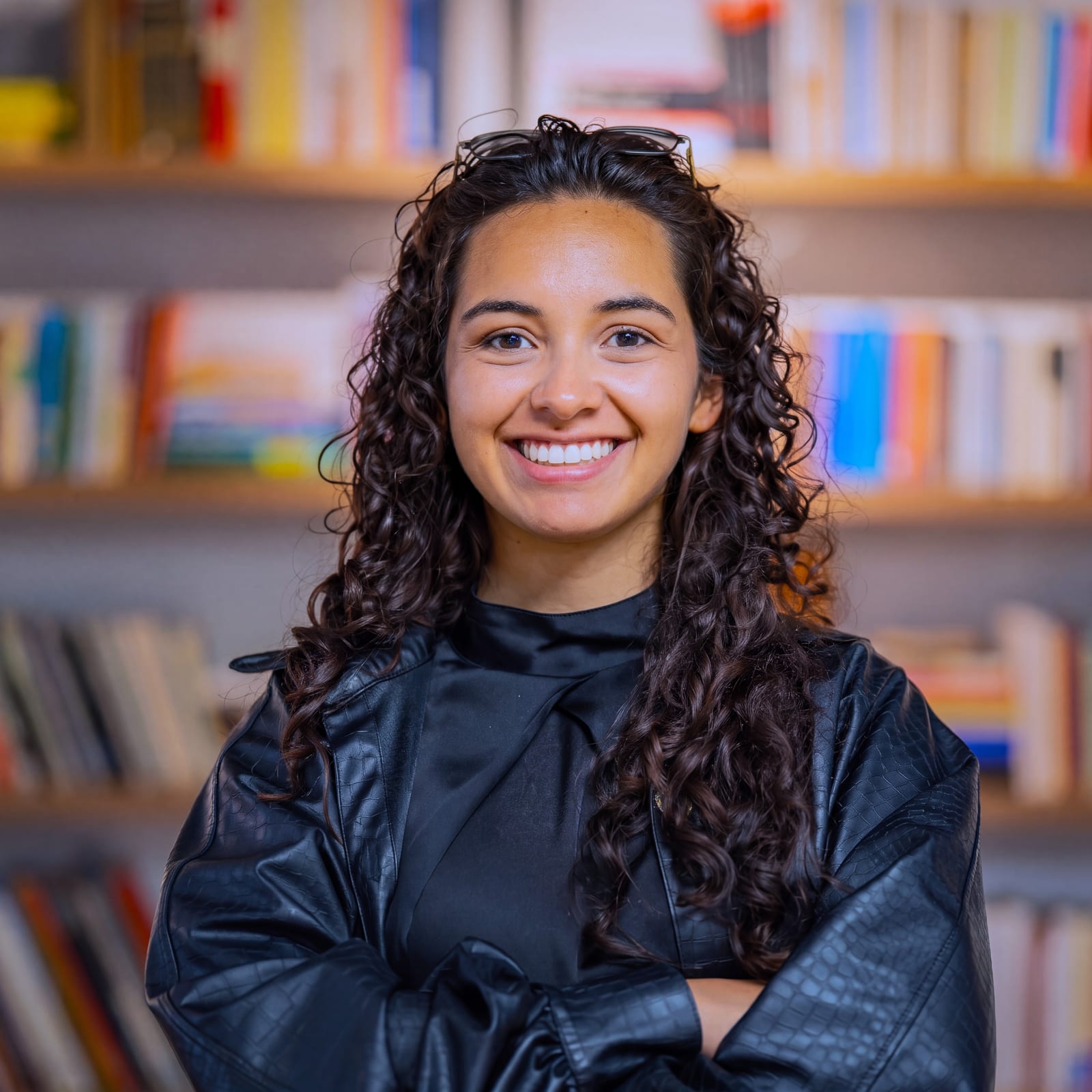 Retrato de Sharon sonriendo, con los brazos cruzados frente a una biblioteca.